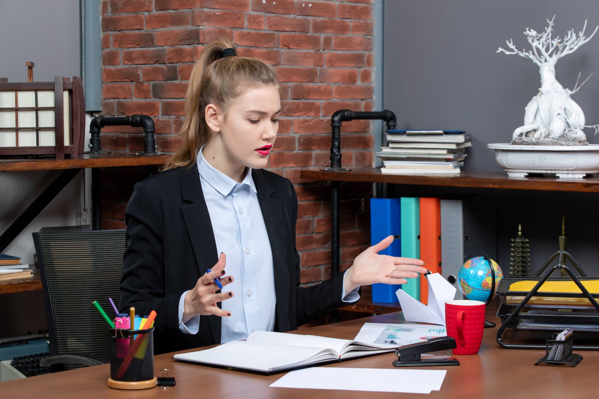 A young female lawyer sitting at a desk with legal documents, gesturing while discussing a case.
