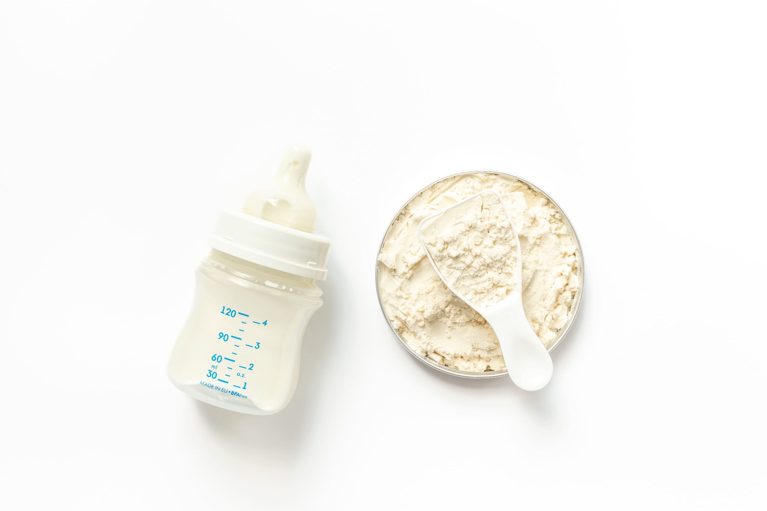 Baby formula powder with a scoop and a baby bottle filled with milk on a white background. Lawsuits claim certain formula brands are linked to necrotizing enterocolitis (NEC) in preterm infants.