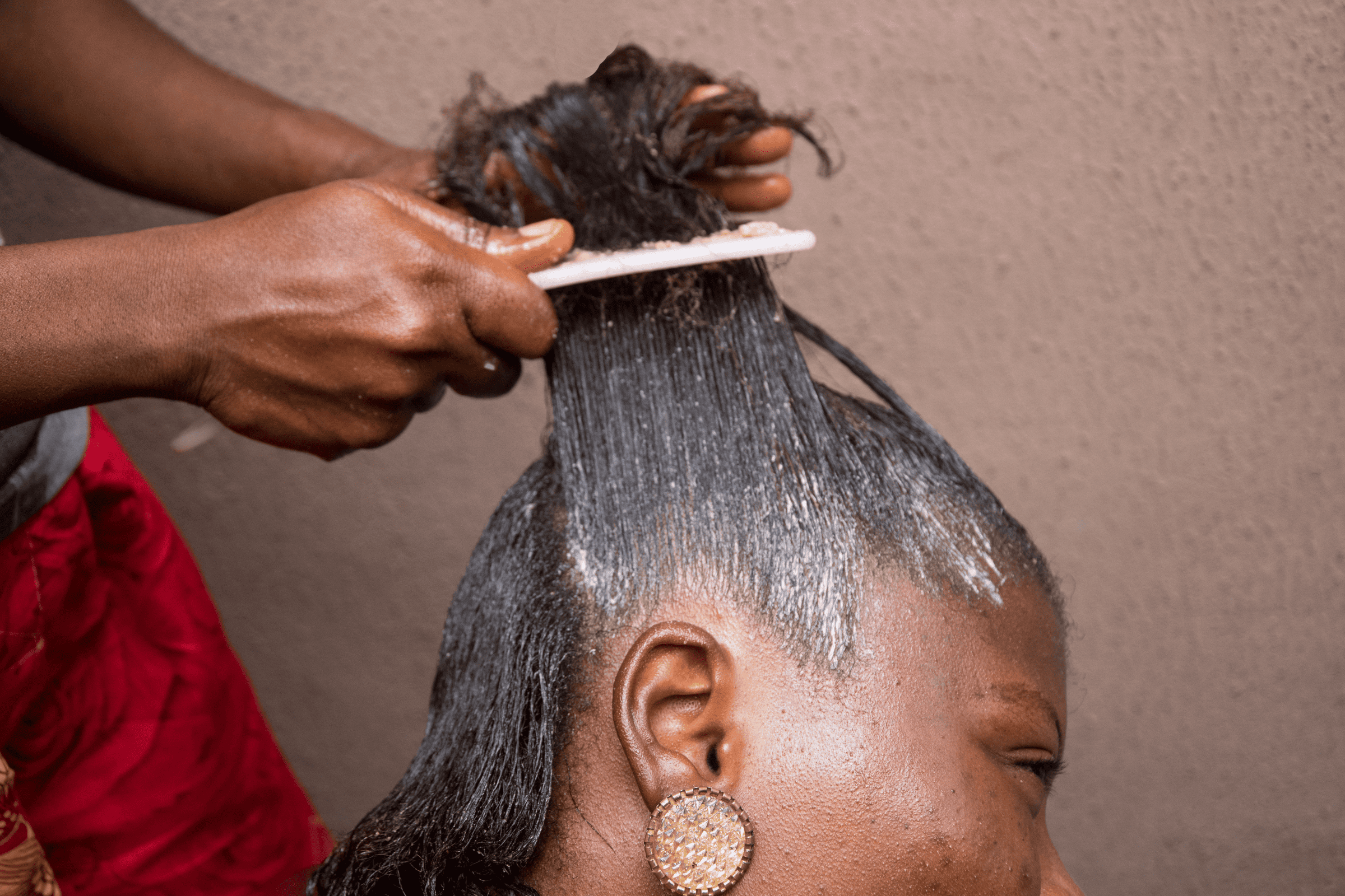 Hairdresser applying chemical hair relaxer to a woman's hair using a comb. Lawsuits claim long-term use of hair relaxers increases the risk of uterine and ovarian cancer.