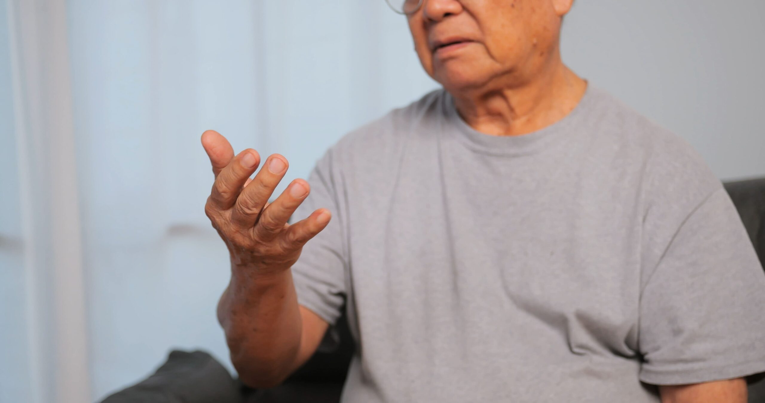An elderly man in a gray shirt looking at his hand, symbolizing the effects of Parkinson’s disease, linked to Paraquat exposure.